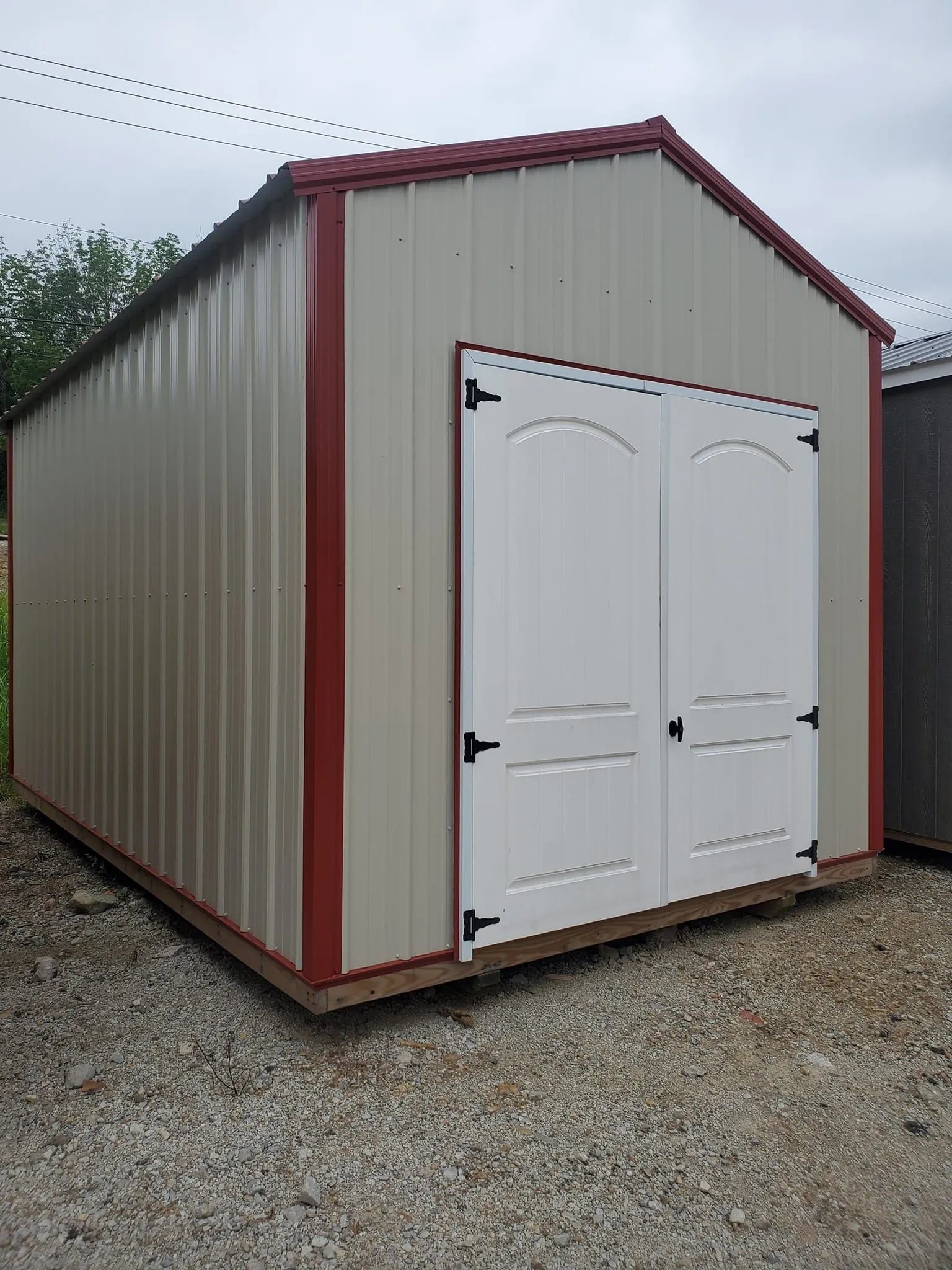 White and red metal storage shed with double doors on gravel ground
