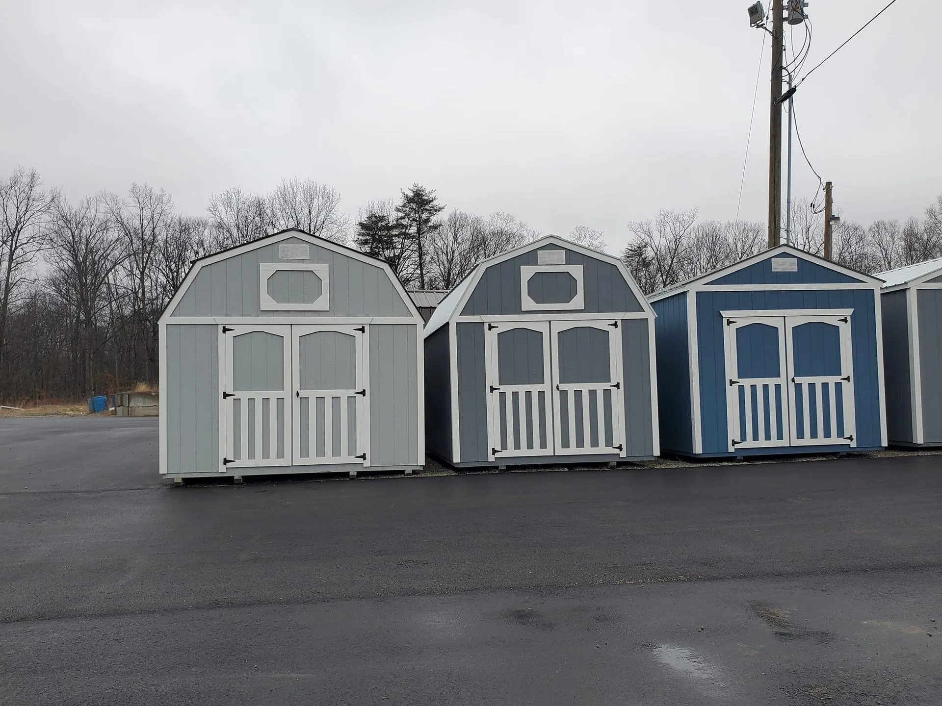 Three storage sheds in gray and blue colors parked on an empty lot