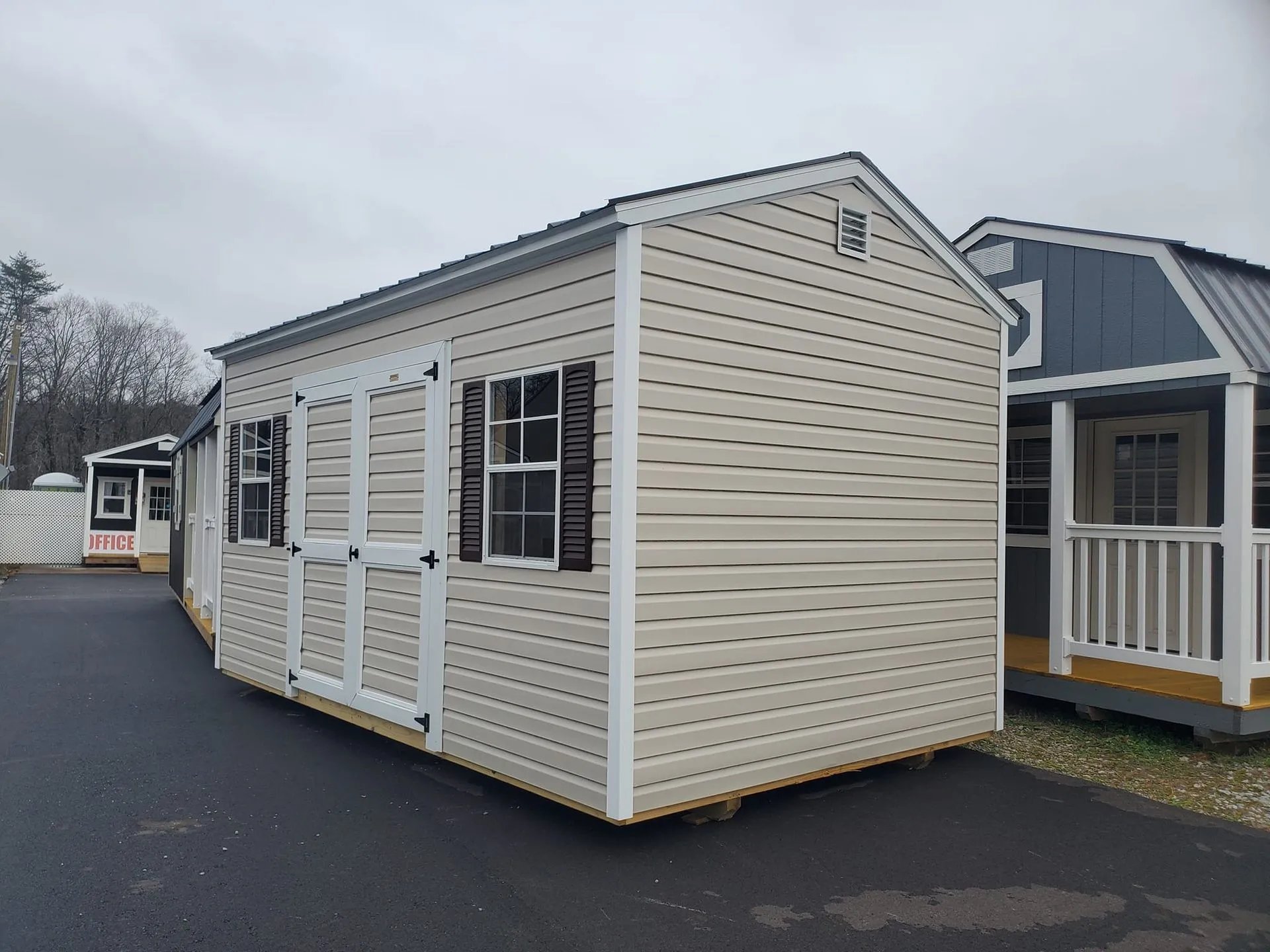 White vinyl-sided storage shed with dark shutters in parking lot