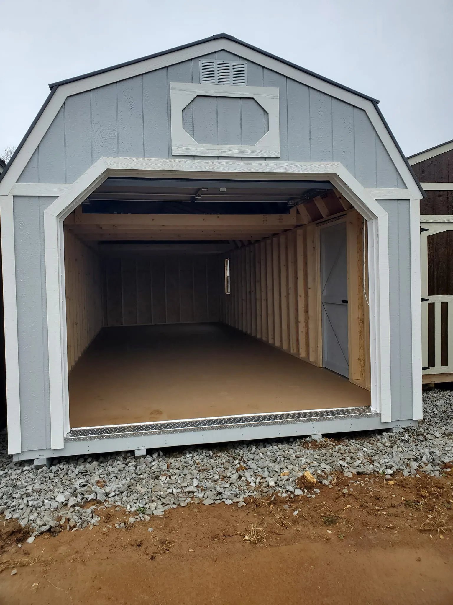 Empty gray storage shed with open doors on gravel ground