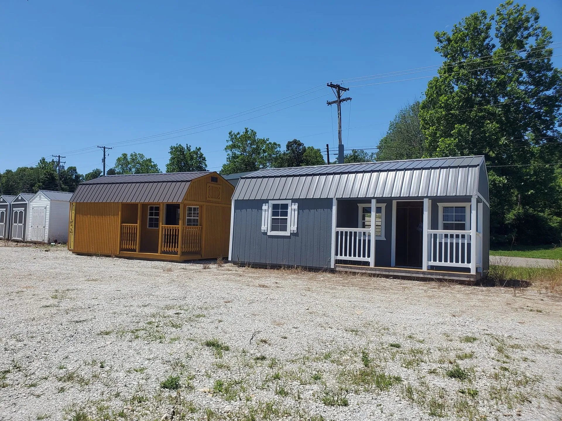 Two portable sheds with porches in yellow and gray on gravel lot