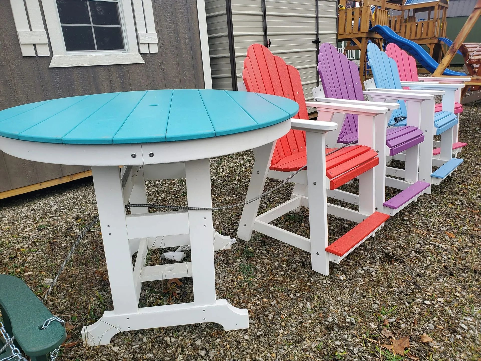 Colorful Adirondack chairs and round table on gravel with playground backdrop